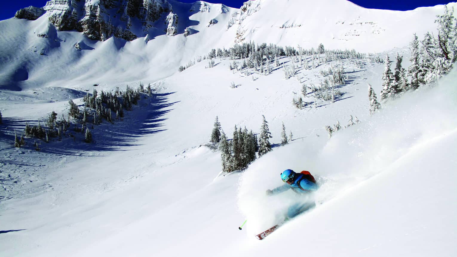 Skier glides down slope, snow spraying around them, on snowy mountain