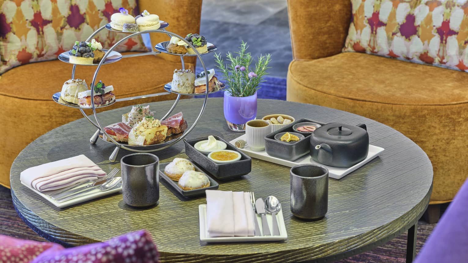 Small round table with contemporary orange and purple club chairs set for afternoon tea service