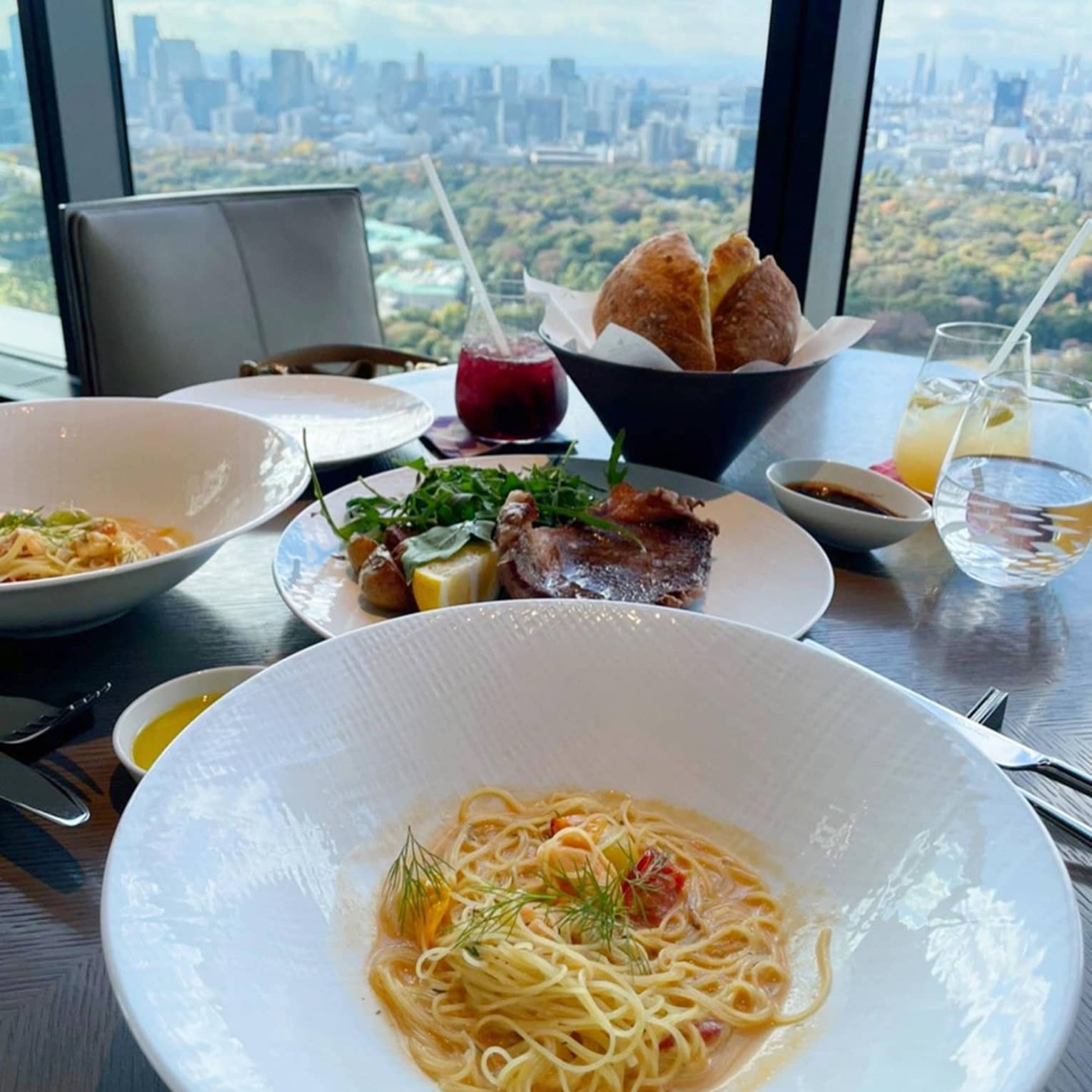 Restaurant table with pasta, steak, bread and drinks overlooking a cityscape