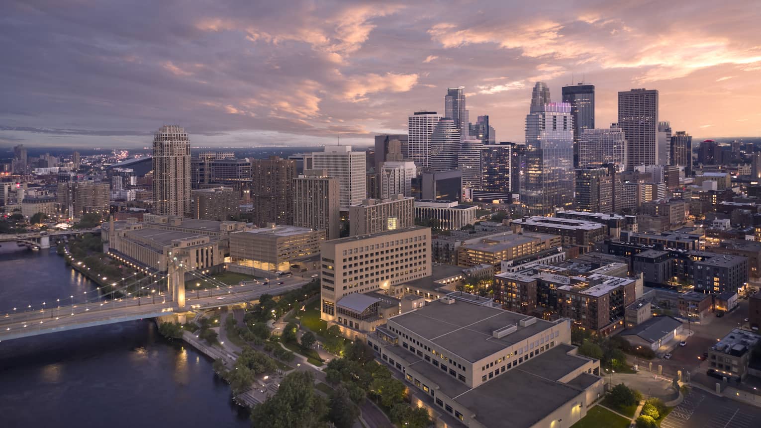 A city during sunset with a bridge crossing a river.