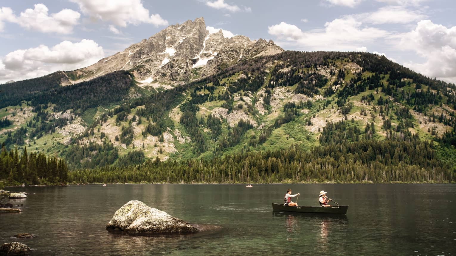 couple drift along in a canoe on a lake in summertime with snowcapped mountains in the background