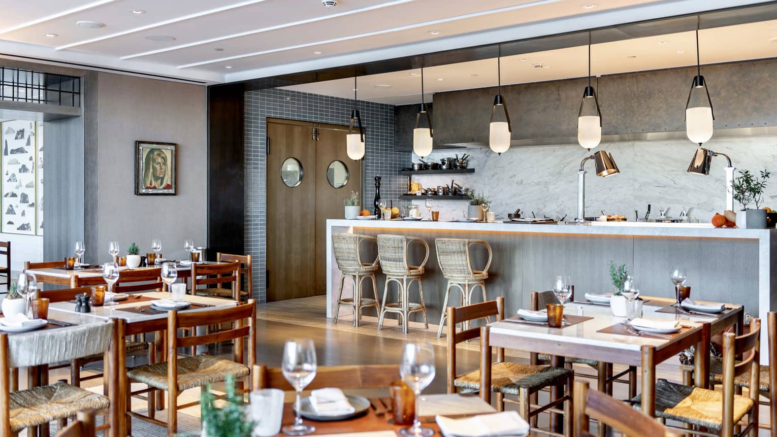 Indoor restaurant with wooden tables and chairs, bar with three wicker seats and pendant lights