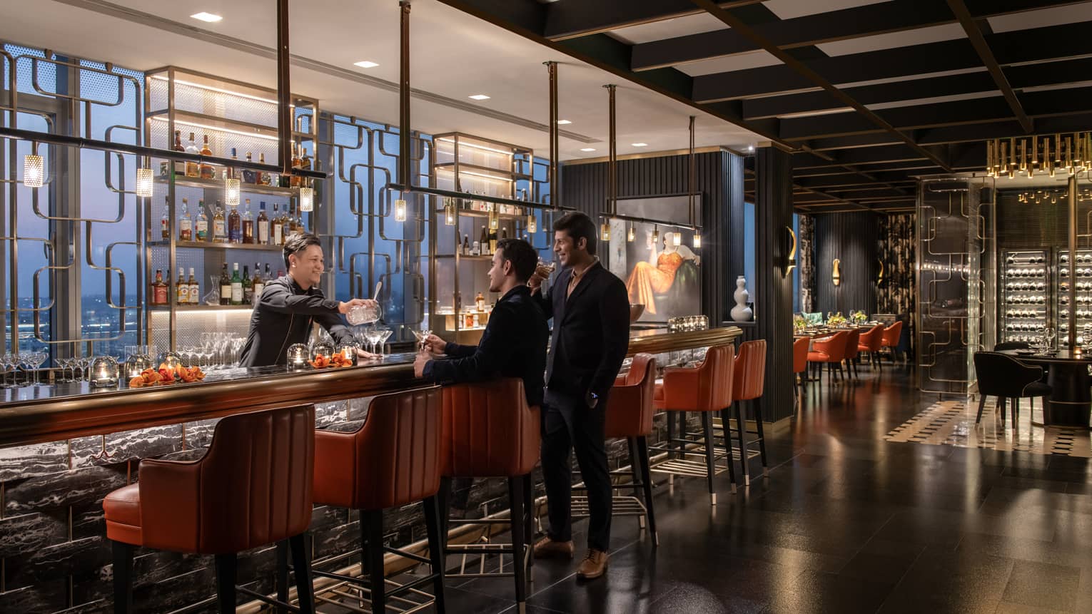 Two people stand at bar as smiling bartender hands them a drink