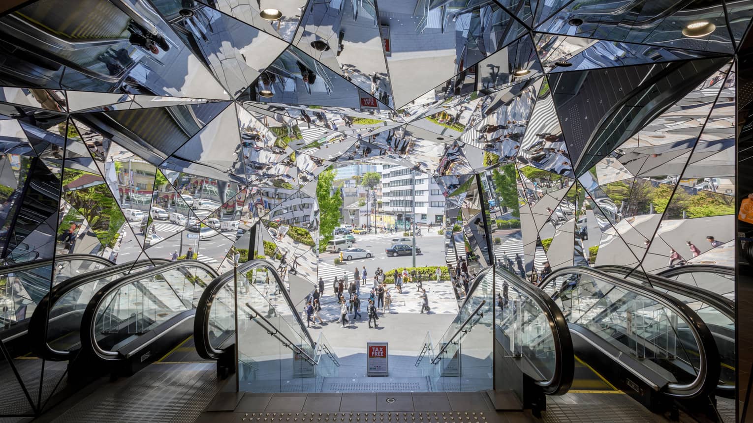 Escalators leading to a mirrored entrance reflecting pedestrians and a busy street scene