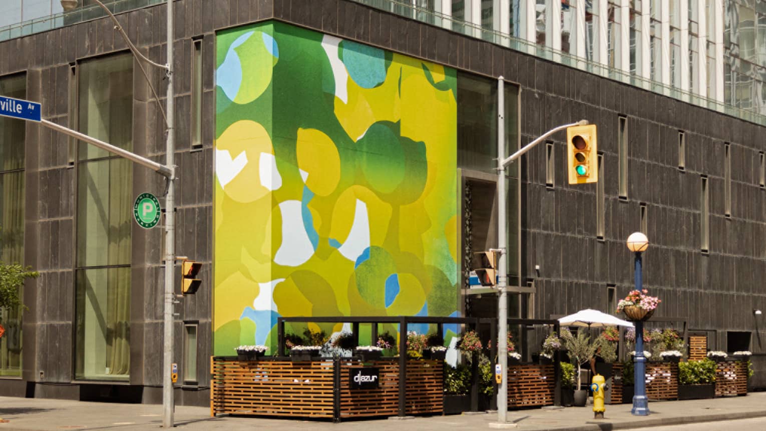 Street corner of the Four Seasons Hotel featuring a bright yellow-and-green mural next to outdoor seating with flower boxes.