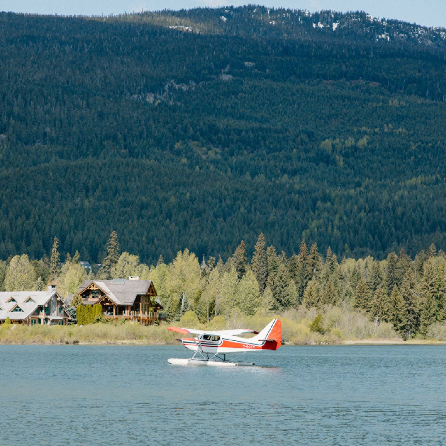 Red and white seaplane glides along the water, mountains visible in background