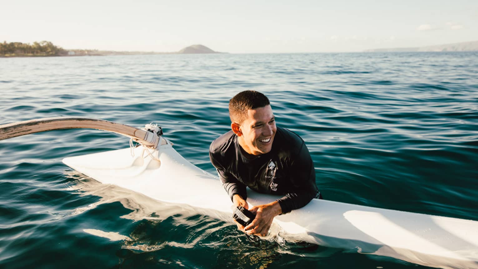 Man rests on an outrigger canoe in the water