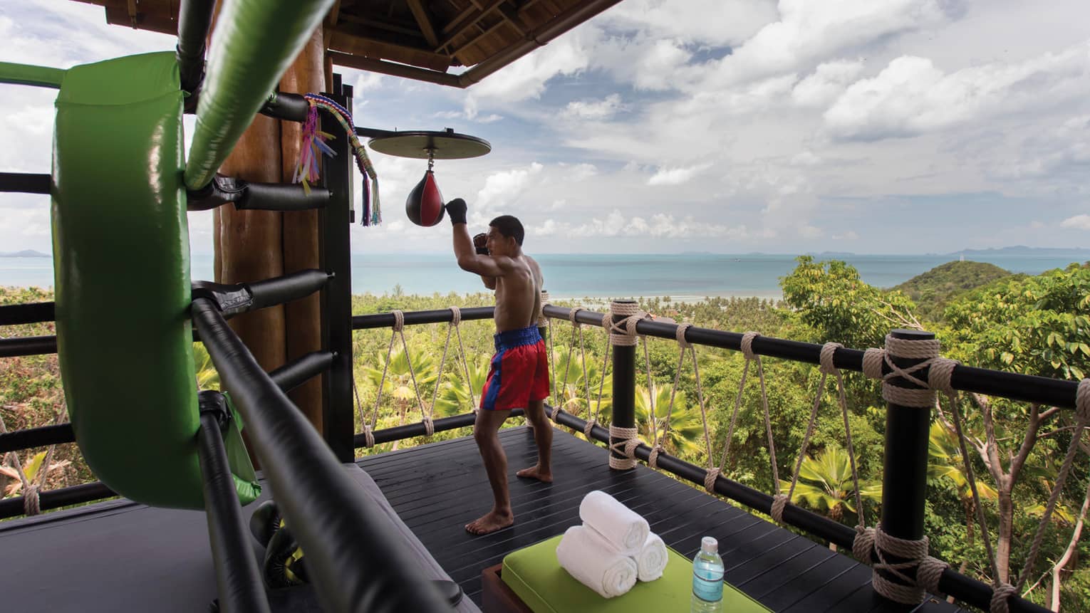 Muay Thai boxer hitting bags on wood deck high up on mountain