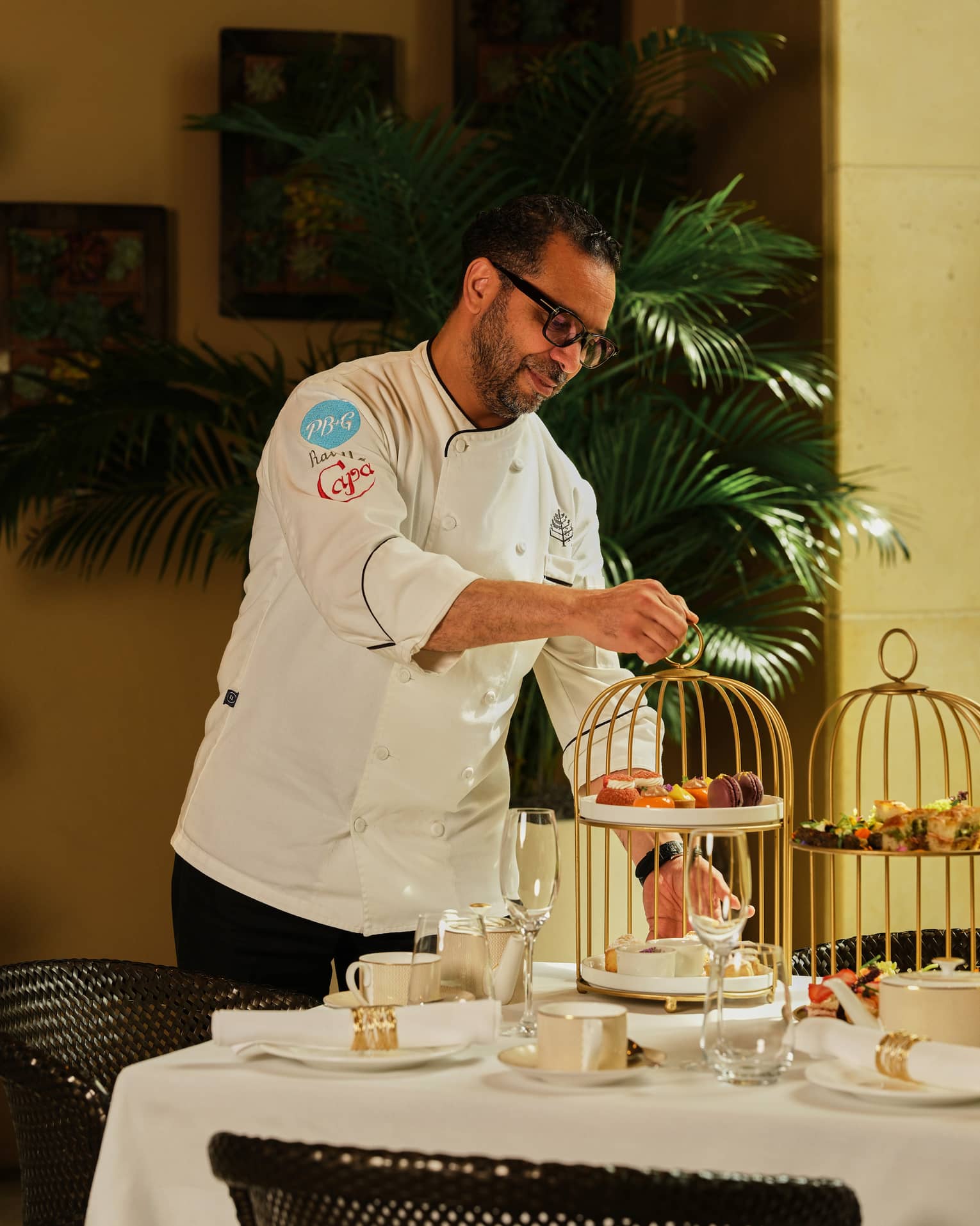 Chef places a tiered tray of pastries onto a table set for afternoon tea