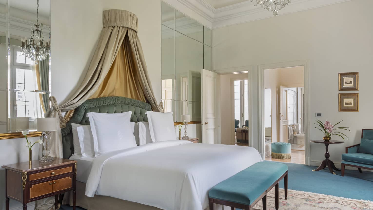 Elegant suite bedroom with king bed, draped canopy, and turquoise velvet bench and chair