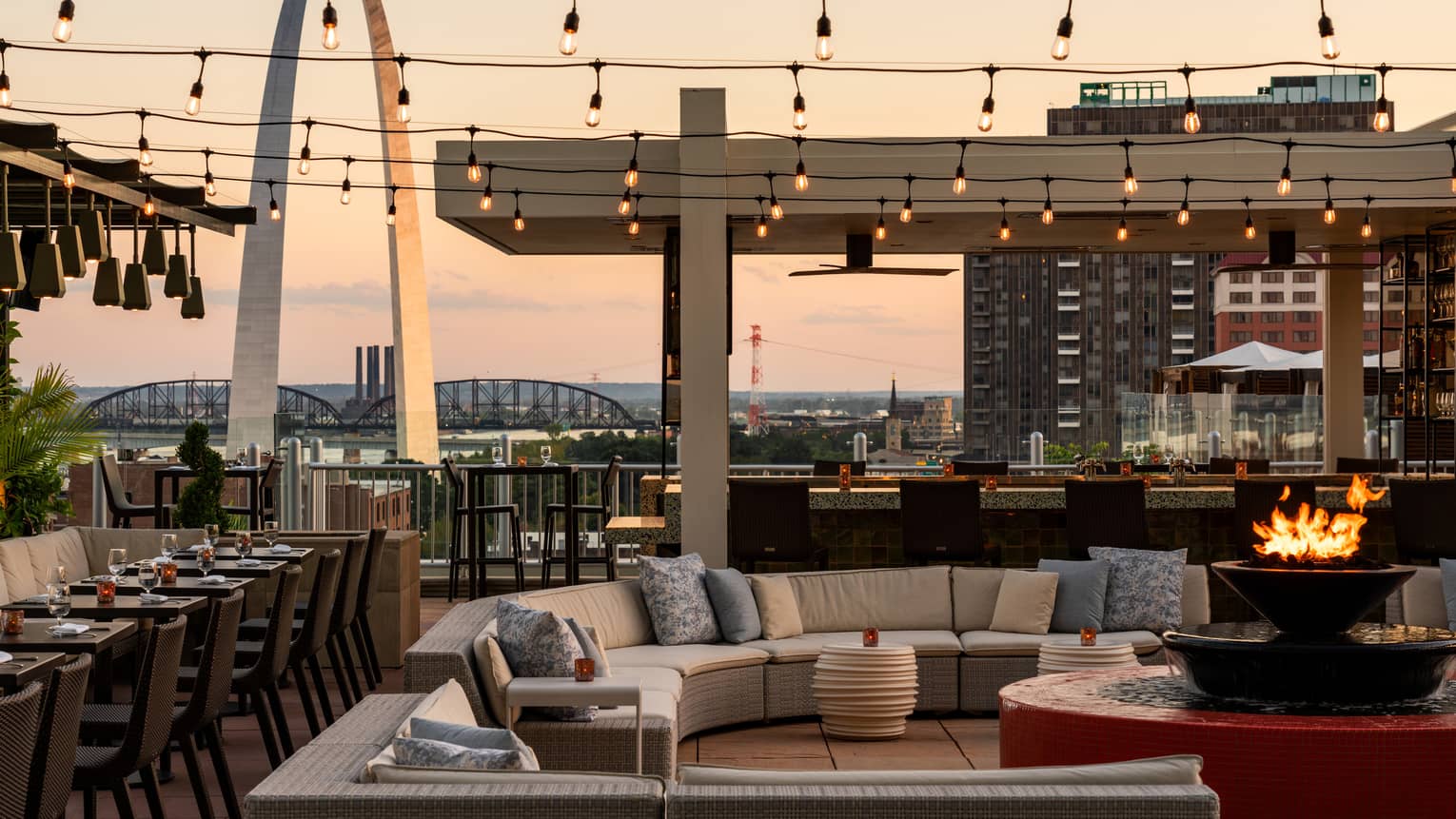 Outdoor terrace with a couch, fire pit, and lights above.
