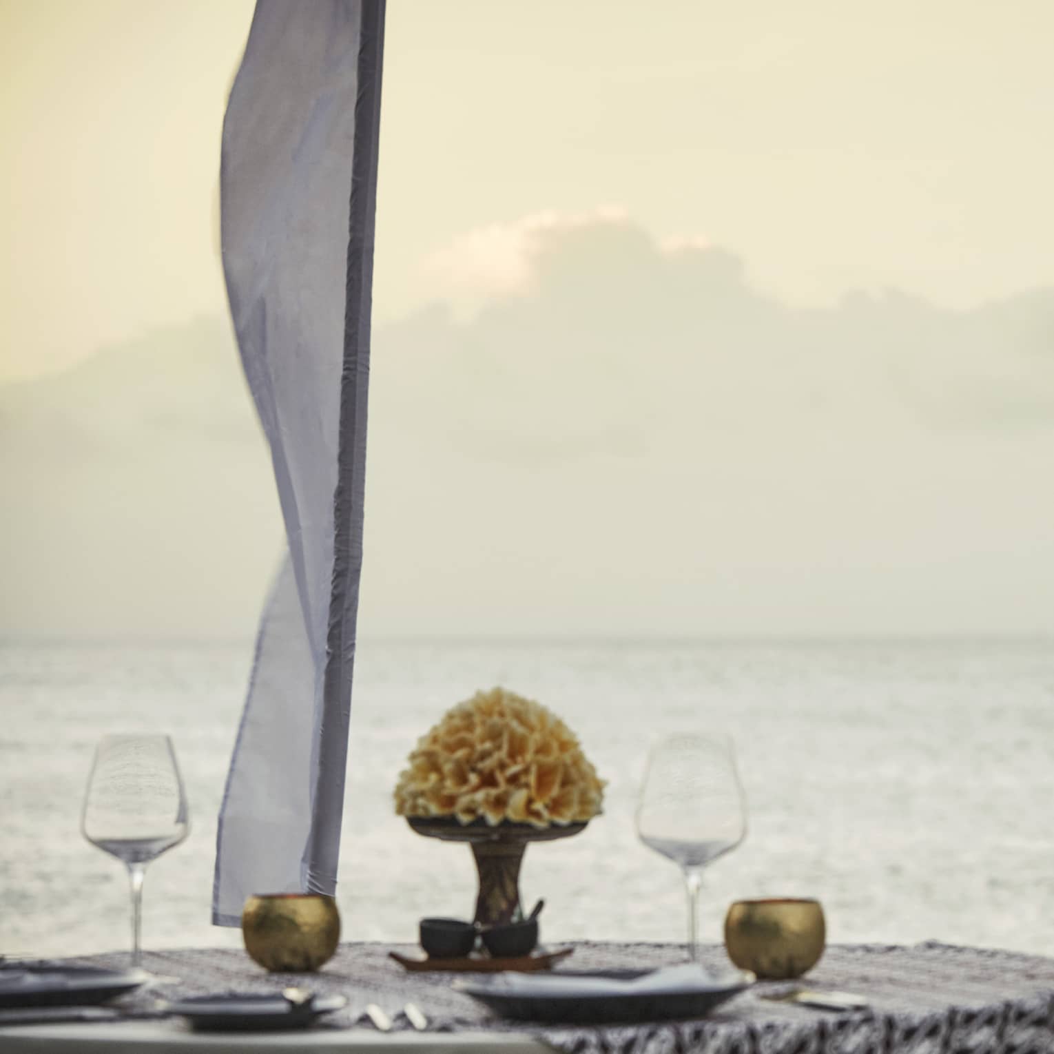 Couple embraces beside private dining table overlooking ocean at sunset