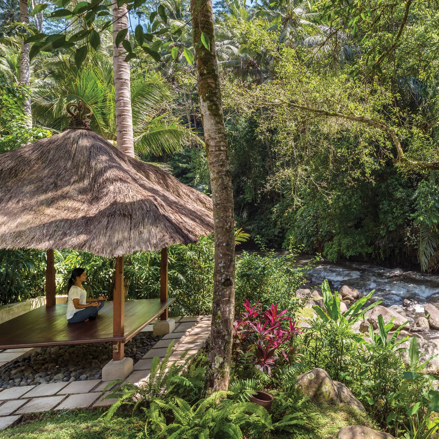 A guest meditating in a pavilion next to a flowing river in Bali