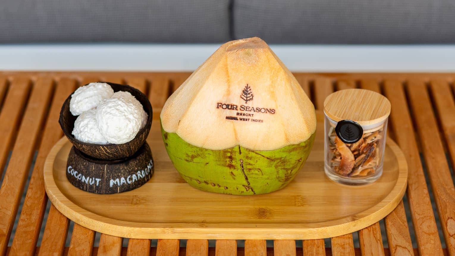 On a wooden platter are coconut macaroons, a fresh coconut carved with the Four Seasons logo and a jar of dried coconut.