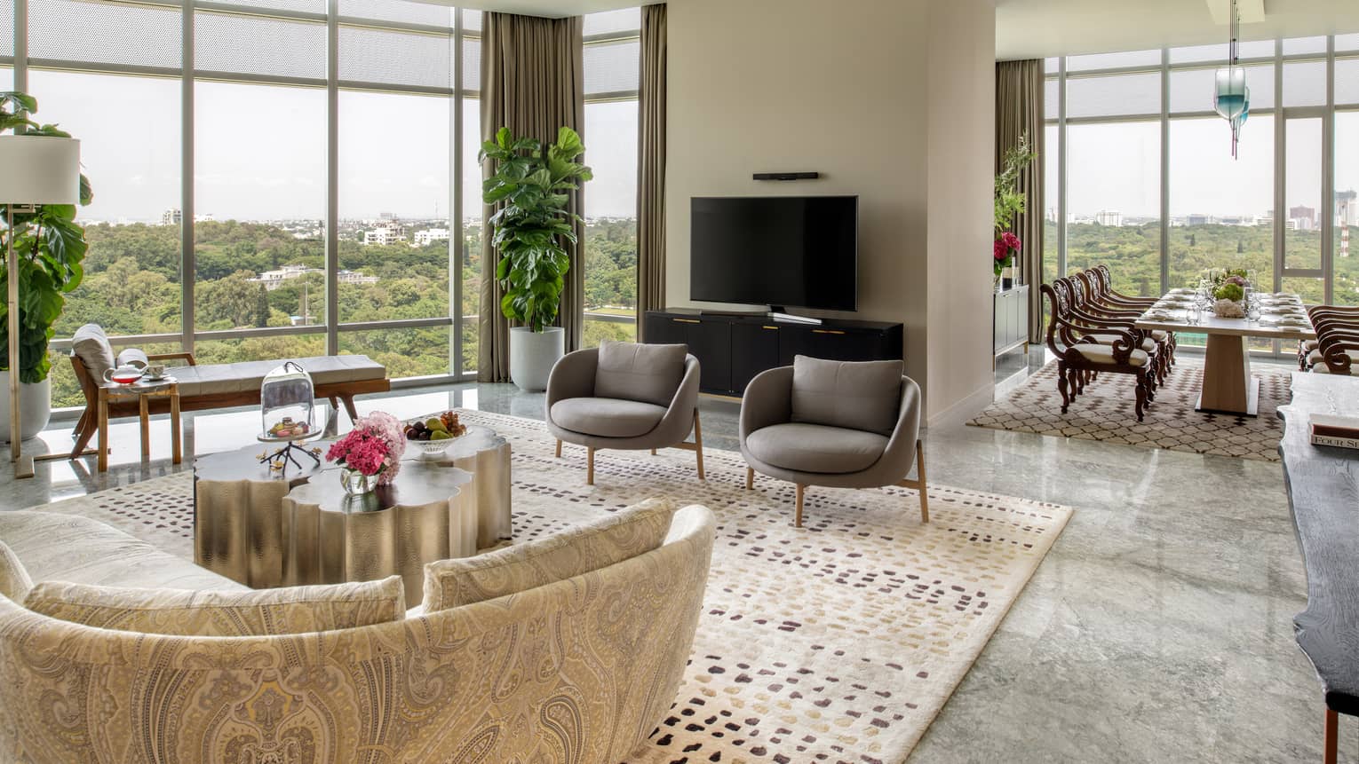 Guest room living area with patterned sectional sofa, grey armchairs, floor-to-ceiling windows, doorway to dining area with long rectangular table