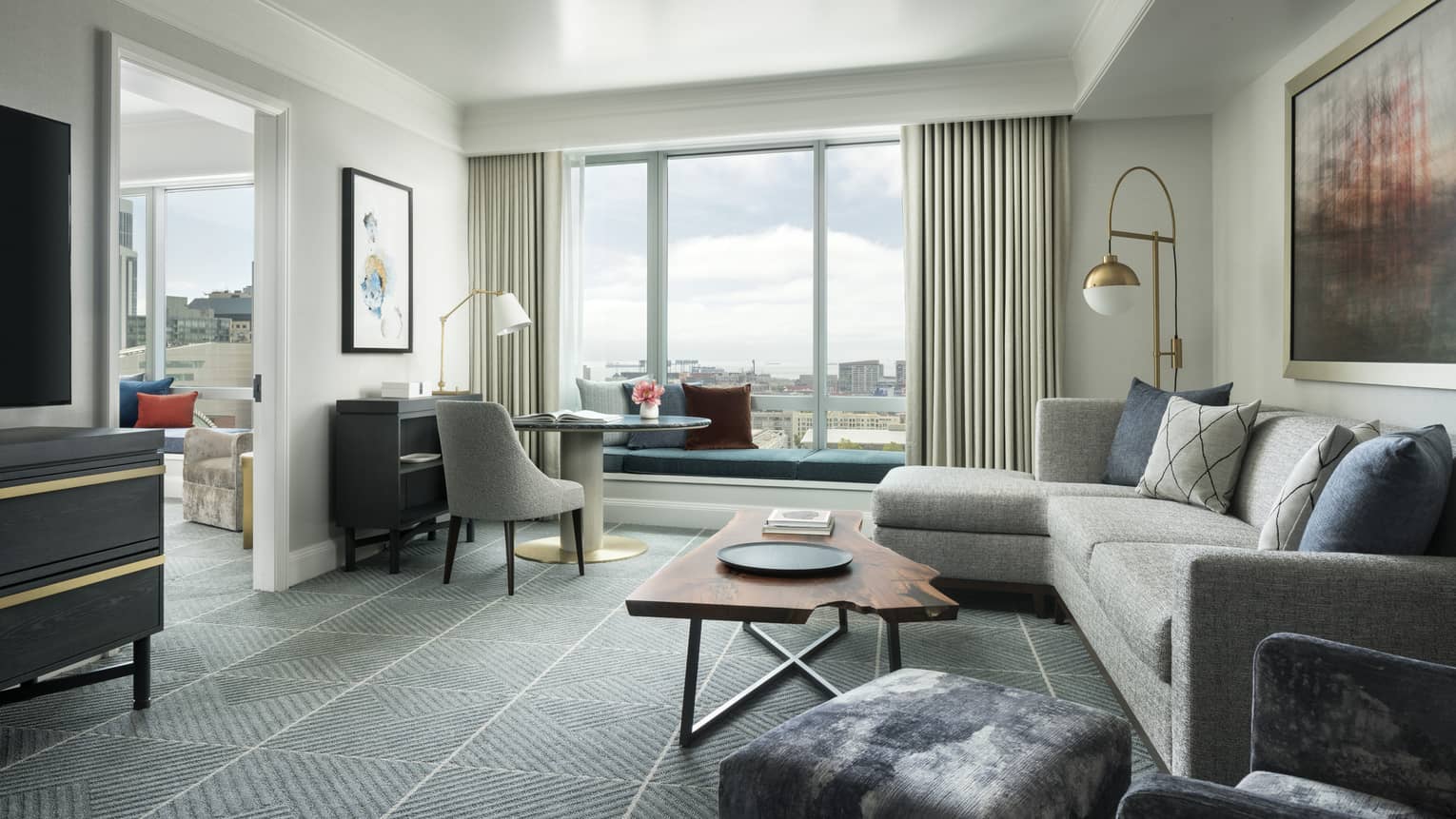 Hotel suite separate living room with retro-style L-shaped grey sofa and desk chair, live-edge wood coffee table