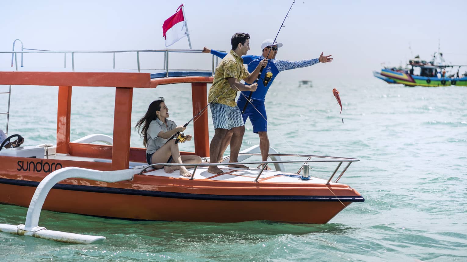 Tour guide teaches two guests to fish on a traditional jukung fishing boat on the open ocean