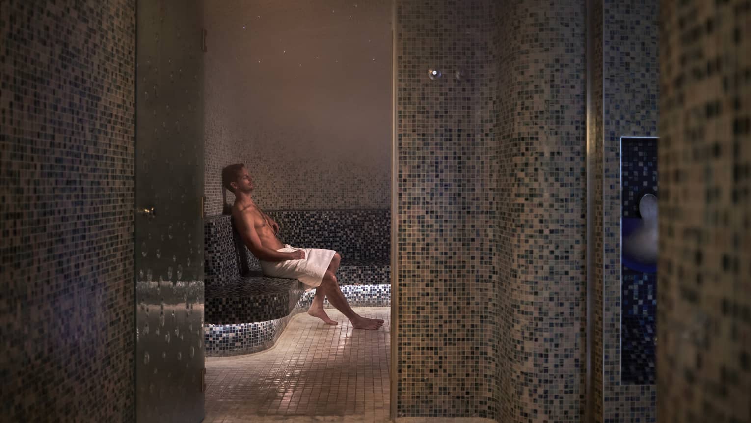 A man sitting with a towel in a dimly lit spa room.