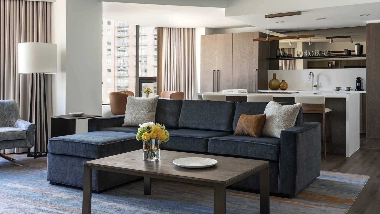 Living room with dark grey sofa, wooden coffee table, kitchen in the back