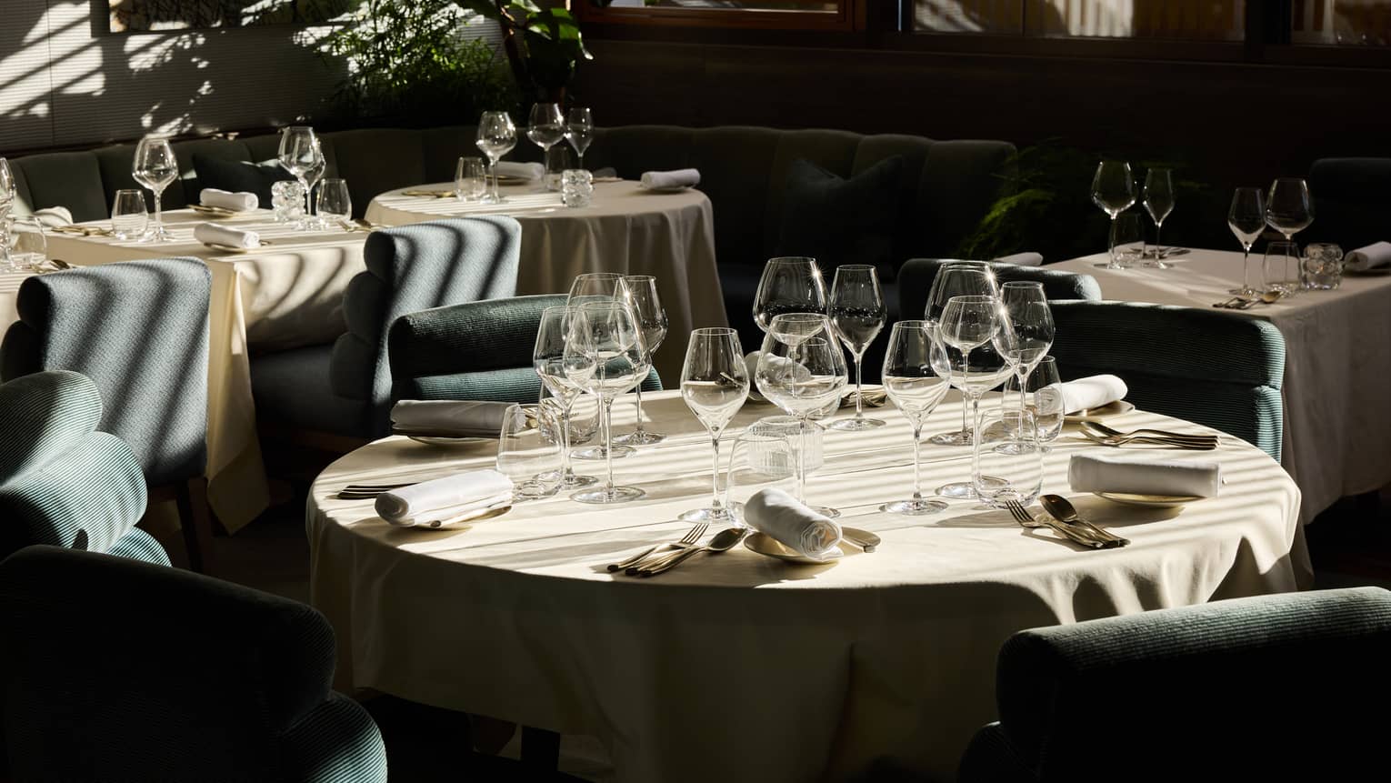 An indoor dining space with dramatic daylight filtering through window blinds and featuring tables, chairs, and place settings for a meal