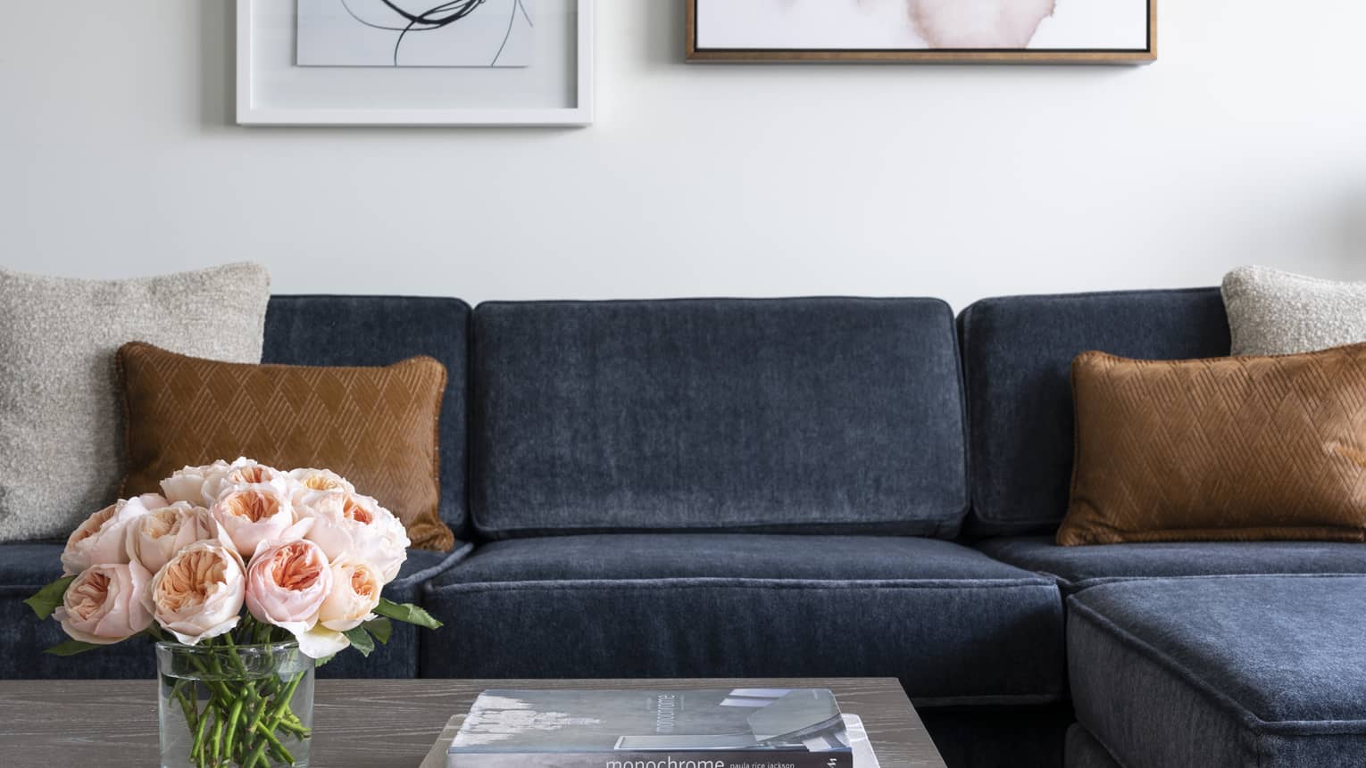 A blue couch near a grey coffee table with books and flowers on it.