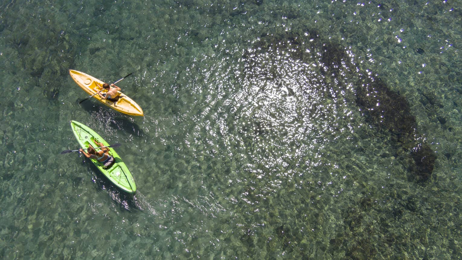 Aerial view of man and woman in green and orange kayaks on reef