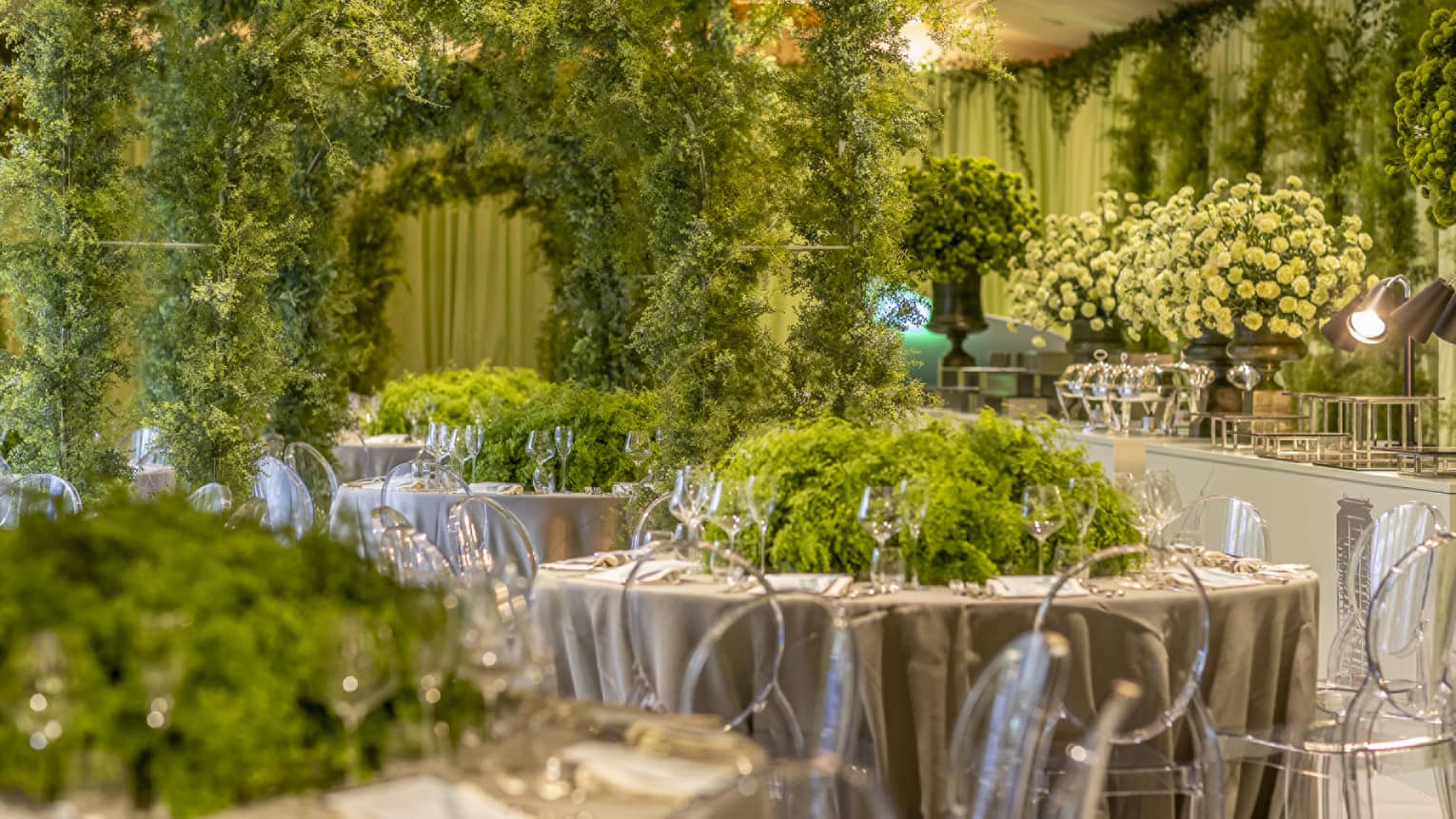Extravagantly decorated event space with round tables with lush green centrepieces and walls of greenery