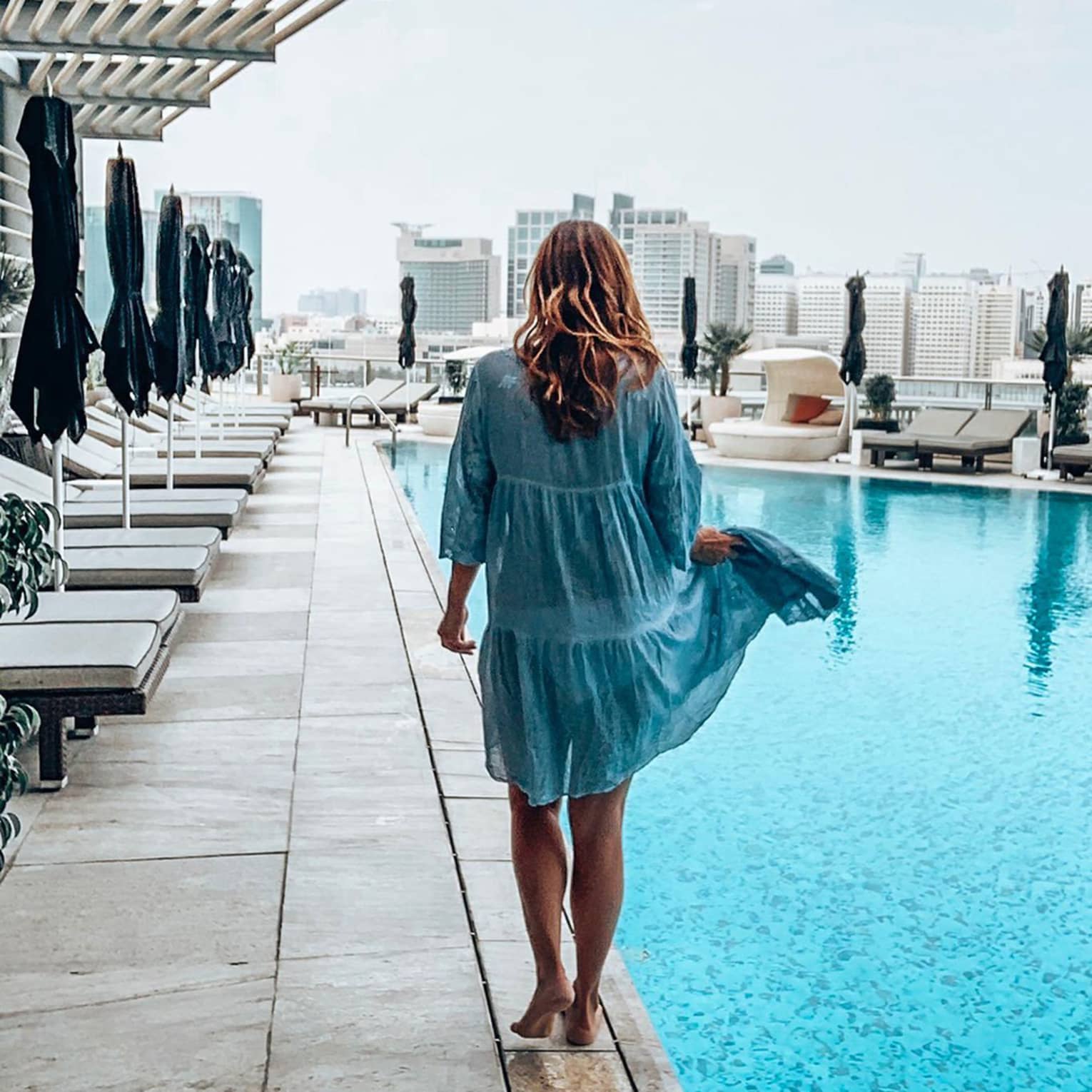 Back of woman walking across outdoor swimming pool deck