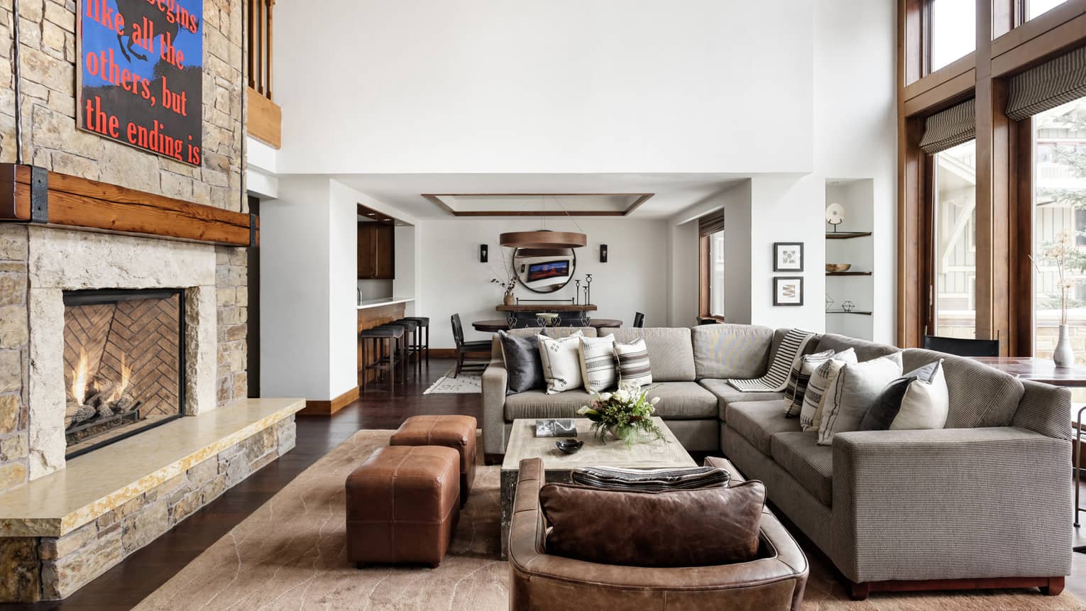 Luxury living room with a stone fireplace, statement art piece, sectional sofa, leather armchair and ottomans, and views of a dining area and bar seating