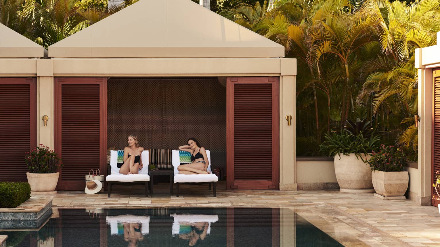 Two women on lounge chairs under poolside cabana