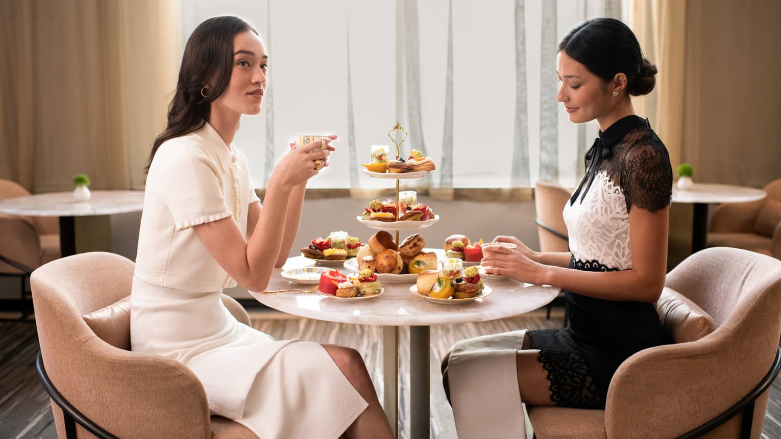 Two guests enjoy a formal tea service including sumptuous sweets and pastries and a three-tiered stand laden with delicacies.