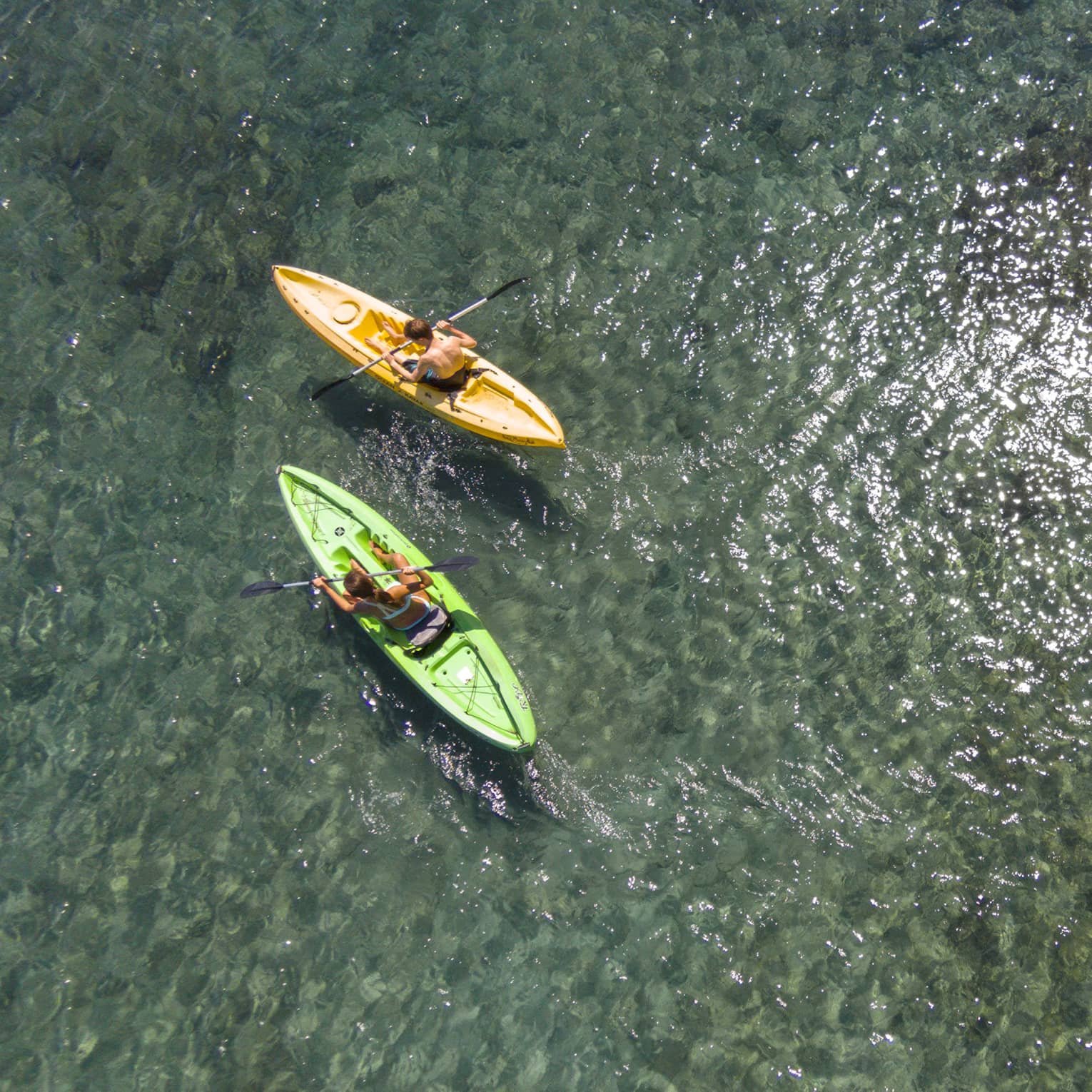 Aerial view of man and woman in green and orange kayaks on reef