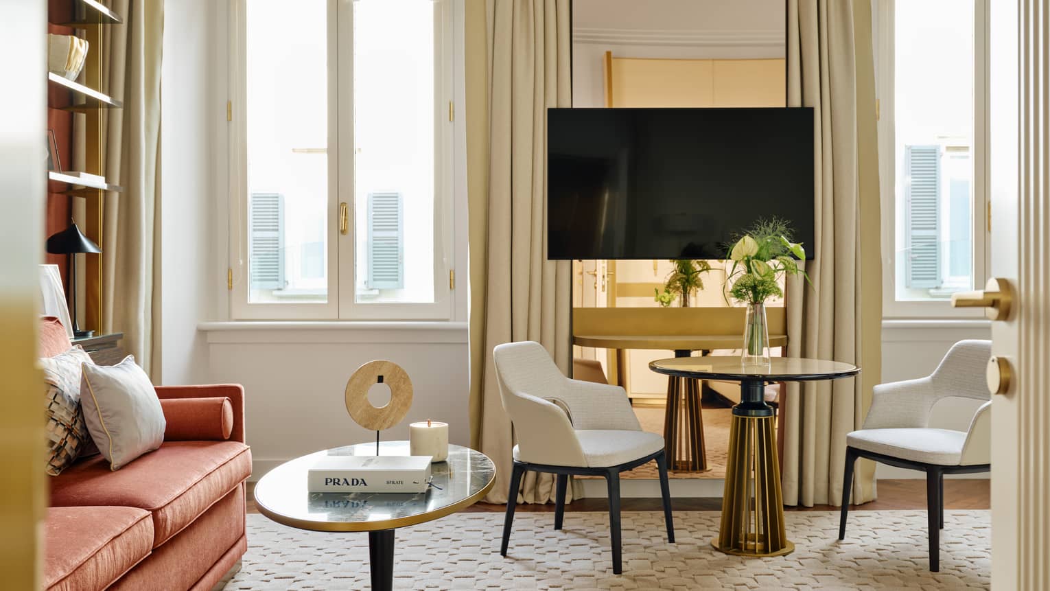 Stylish hotel room featuring a sitting area, with a round table and two chairs, TV, red sofa and windows