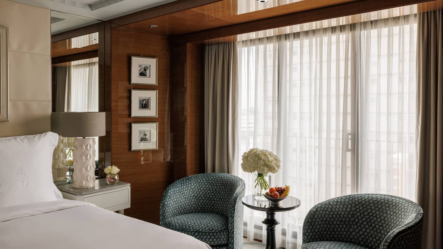 Luxury hotel suite, with a king bed, small table and two chairs but a window with sheer curtains at Four Seasons Hotel London at Park Lane