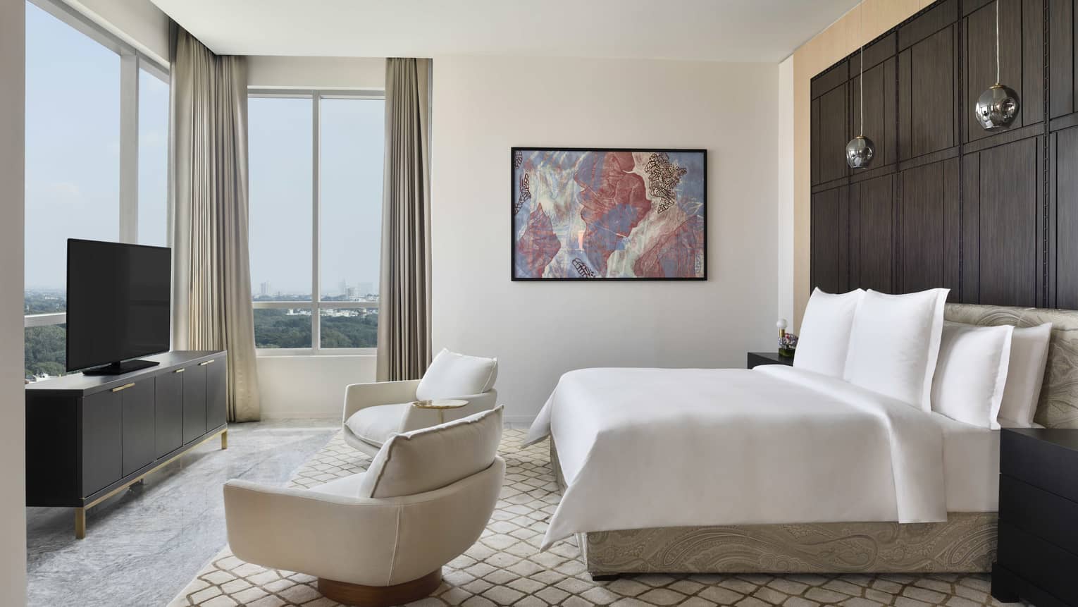 Bedroom with king bed, two arm chairs, TV and windows