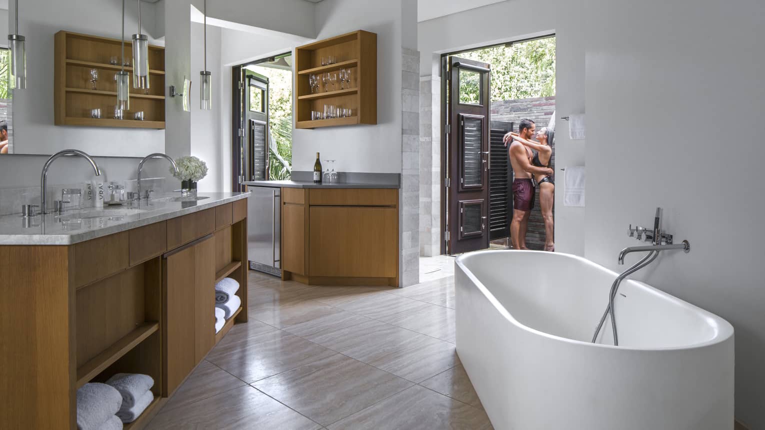 Interior view of small apartment with man and woman in swimsuits embracing in outdoor shower beyond