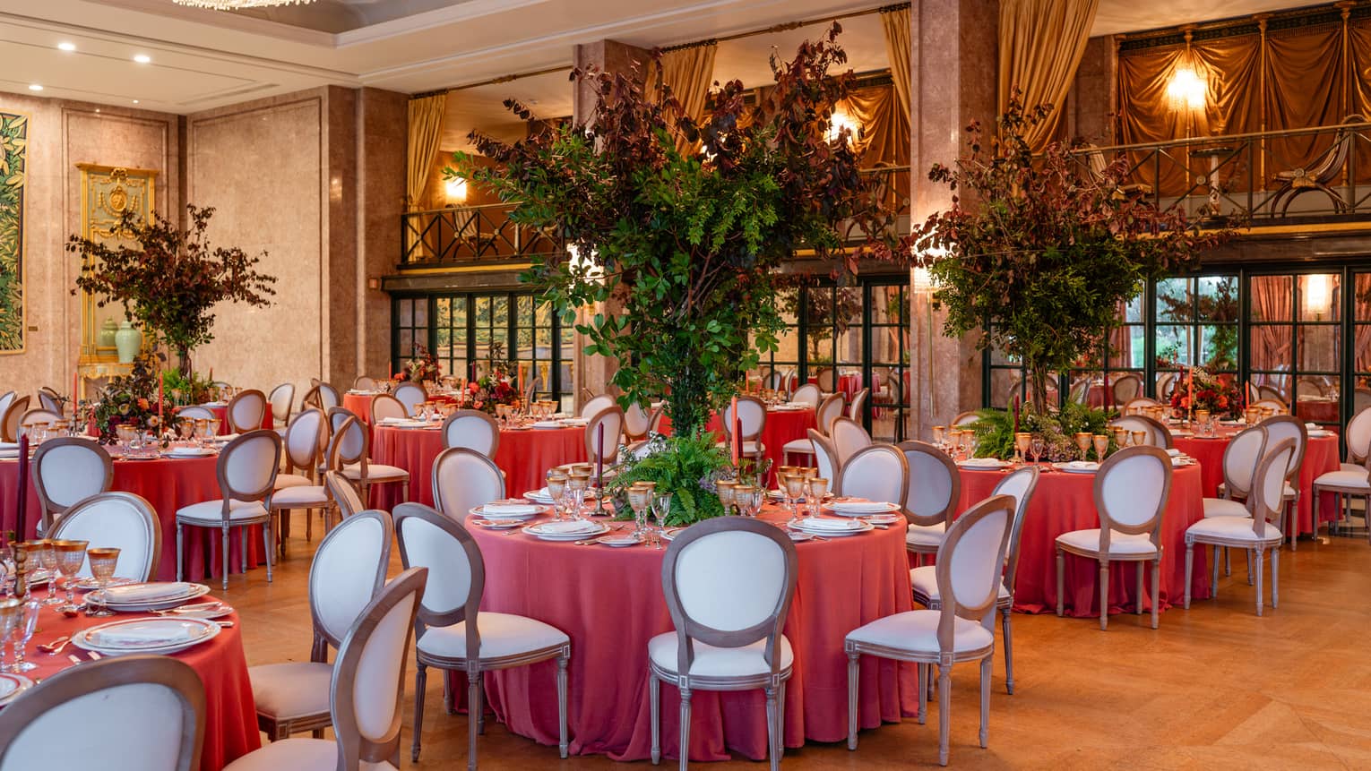 Elegant ballroom set for a formal event, with table rounds featuring coral-coloured tablecloths and tall floral centrepieces