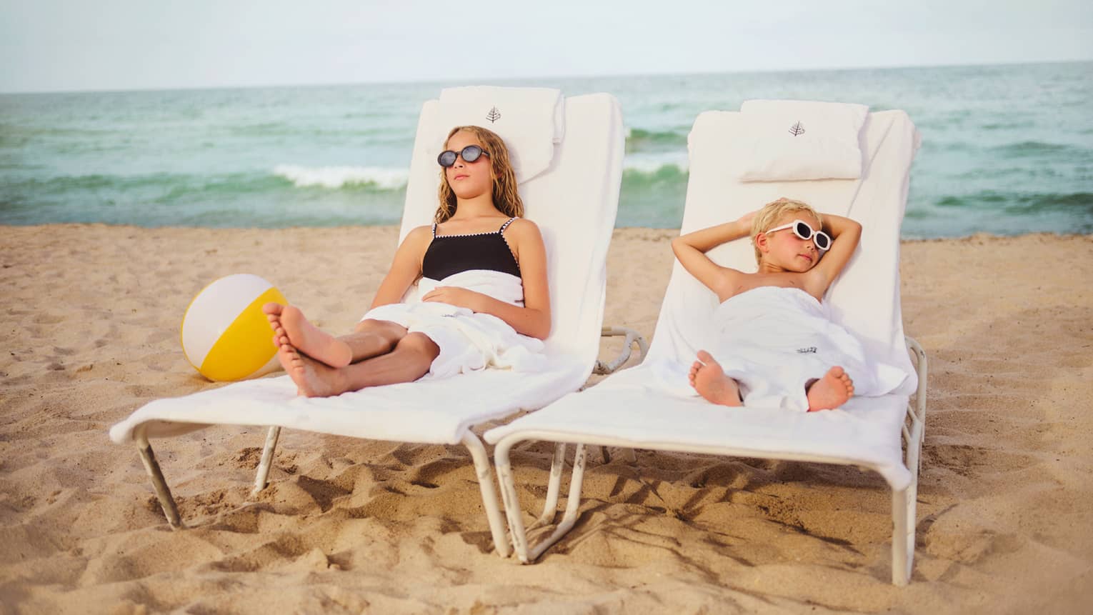 Two young children relax on loung chairs on the beach