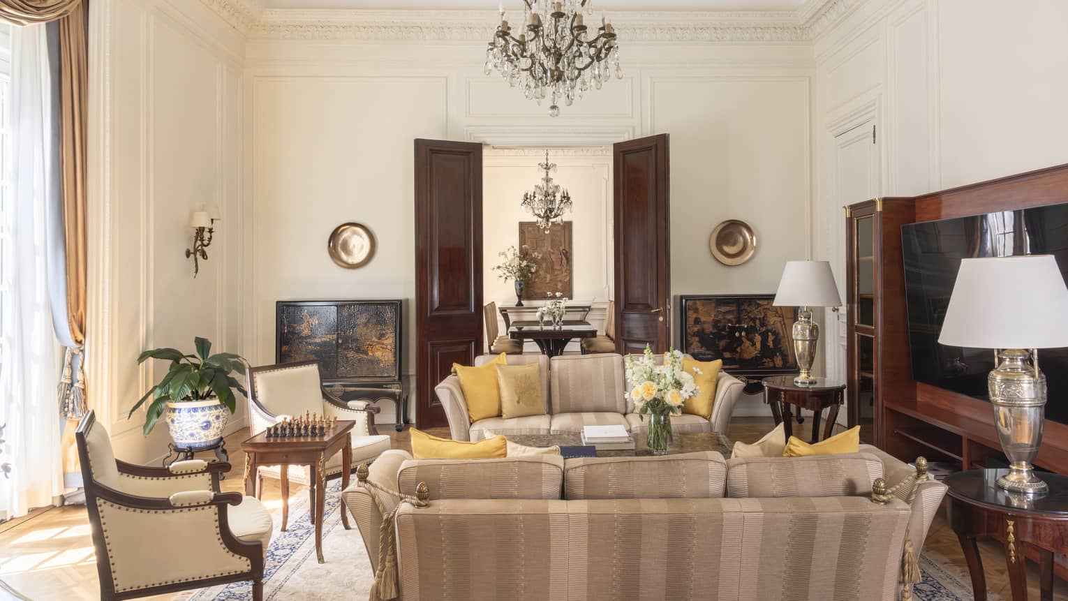 Suite living room with two sofas, two arm chairs, a large entertainment centre and a crystal chandelier