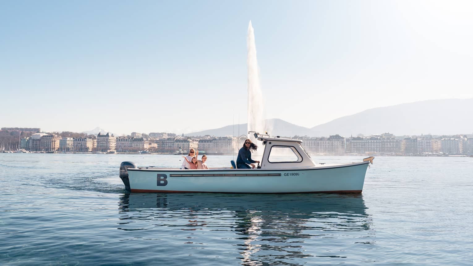 Four people in small boat on Lake Geneva with Jet d'Eau fountain and city in backdrop