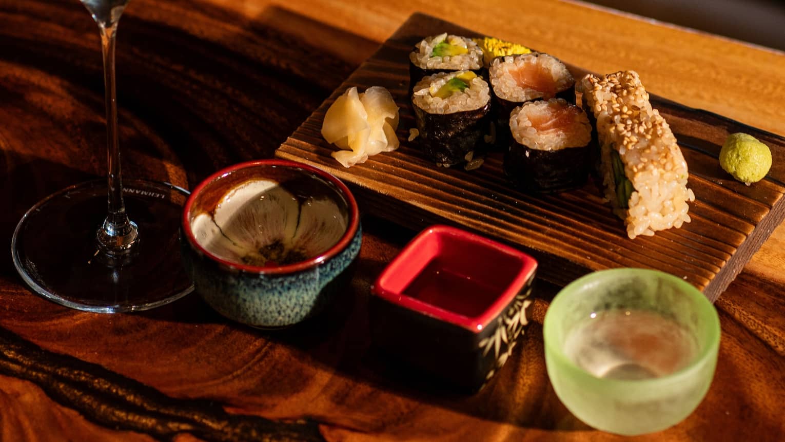 A glass of sake paired with sushi served on a wooden plate with decorate ceramic bowls