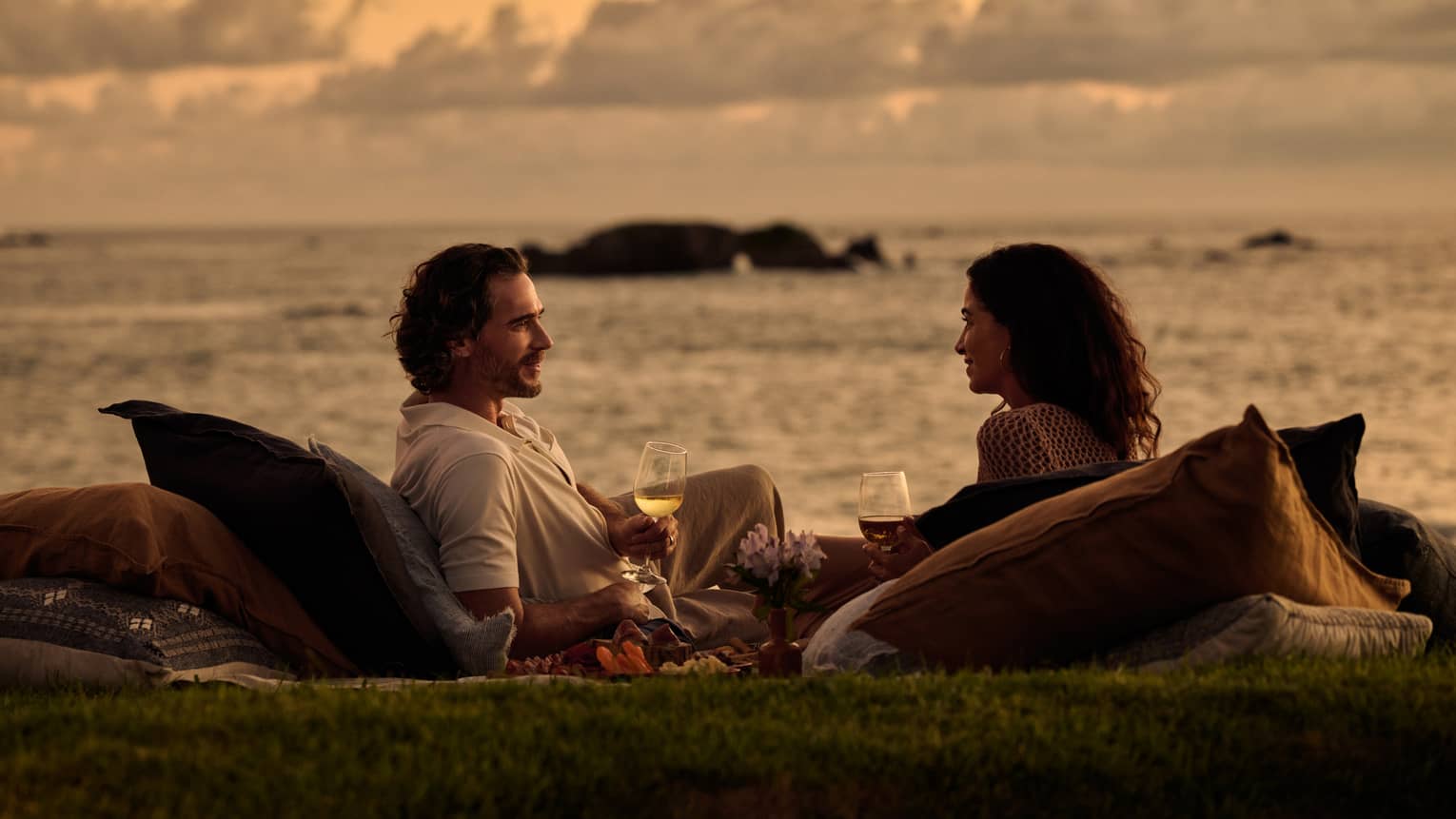 Two people enjoy a sunset picnic next to the ocean.