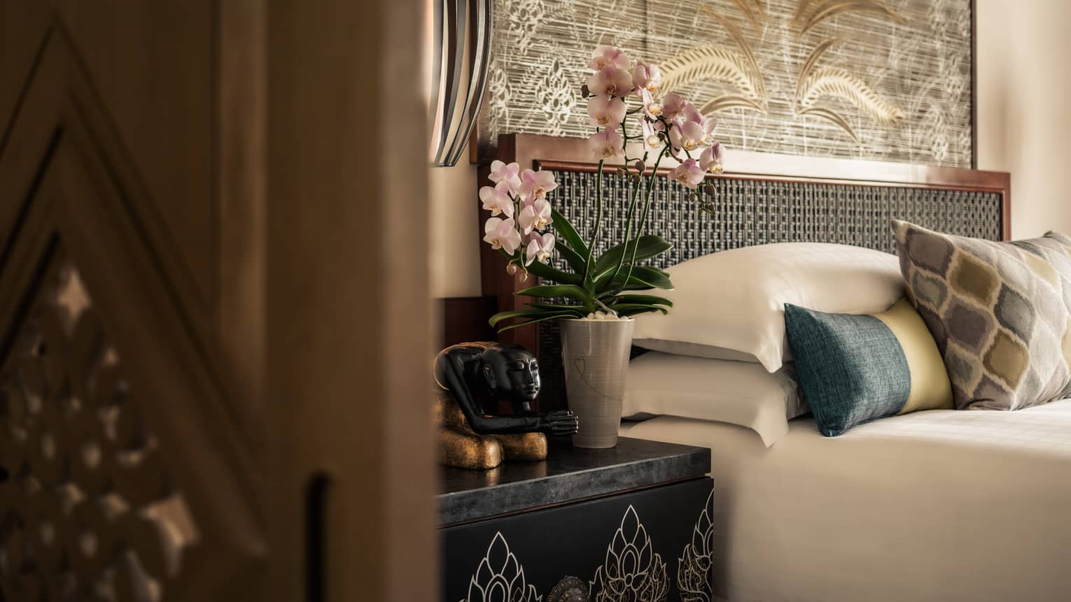 Spa Residence close-up of top of bed with accent pillows, nightstand with tall orchid, black-and-gold statue