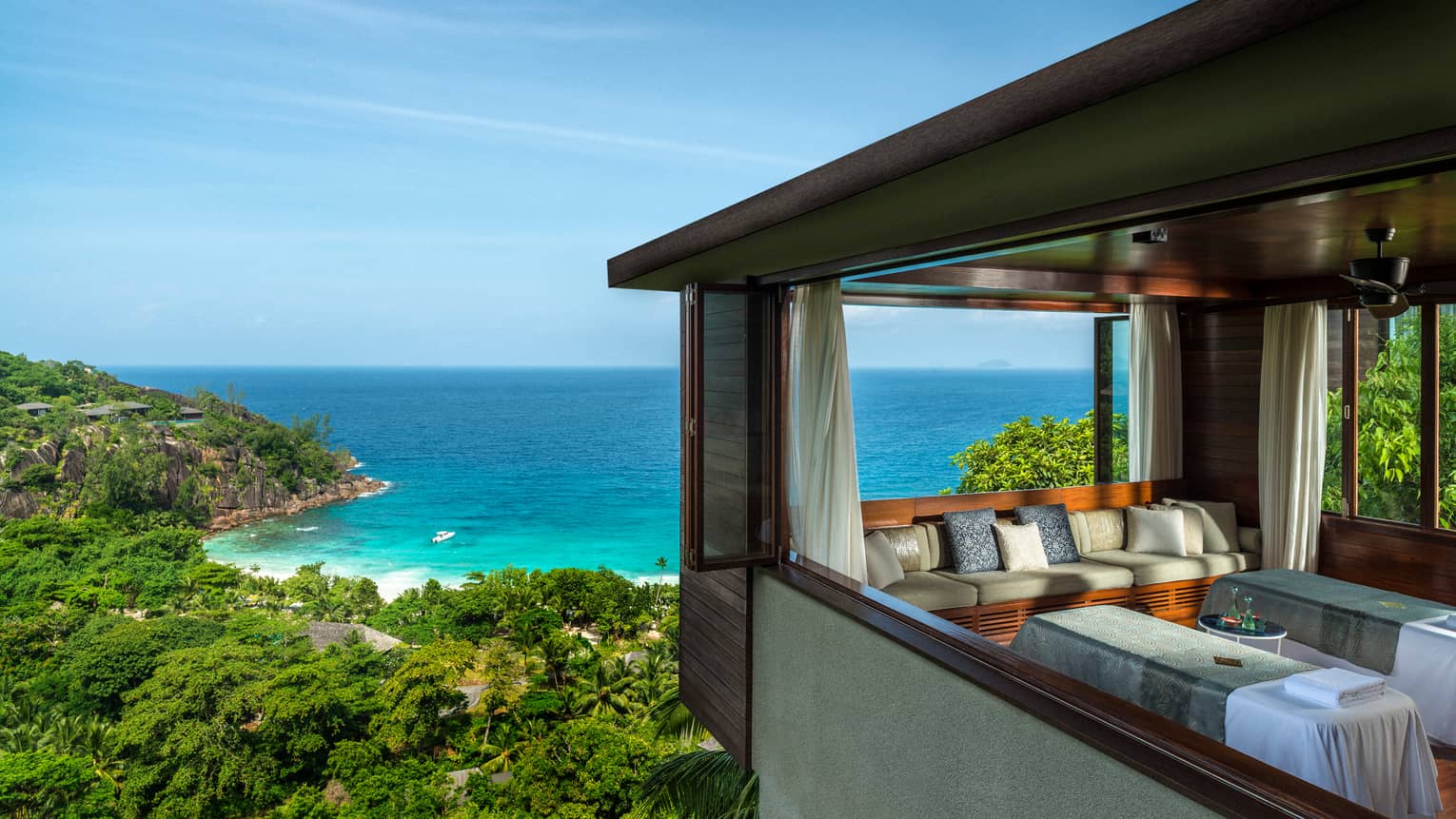 Two side-by-side massage tables in spa room high above trees, ocean
