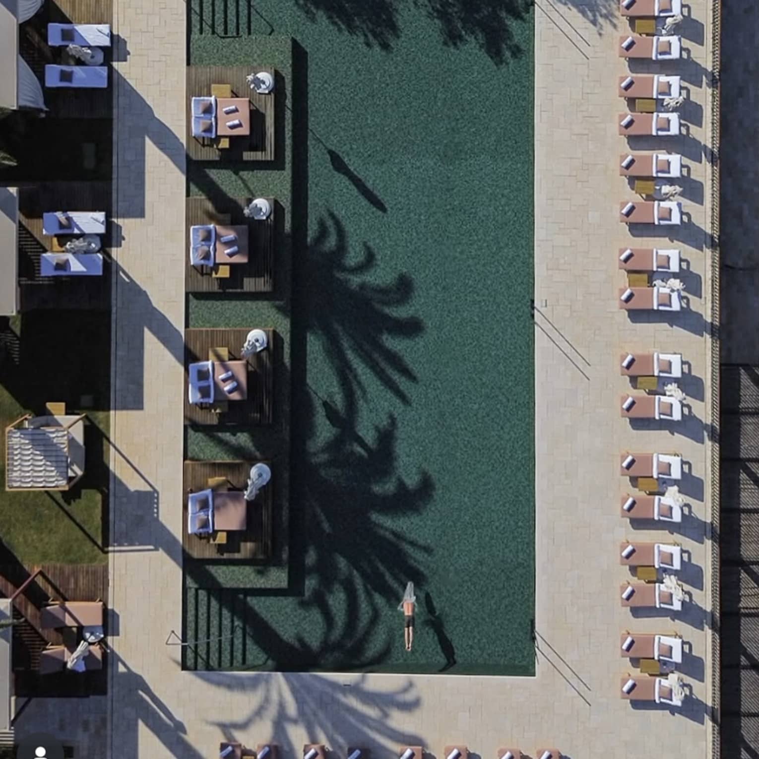 Aerial view of a man swimming in a large outdoor pool surrounded by lounge chairs and cabanas
