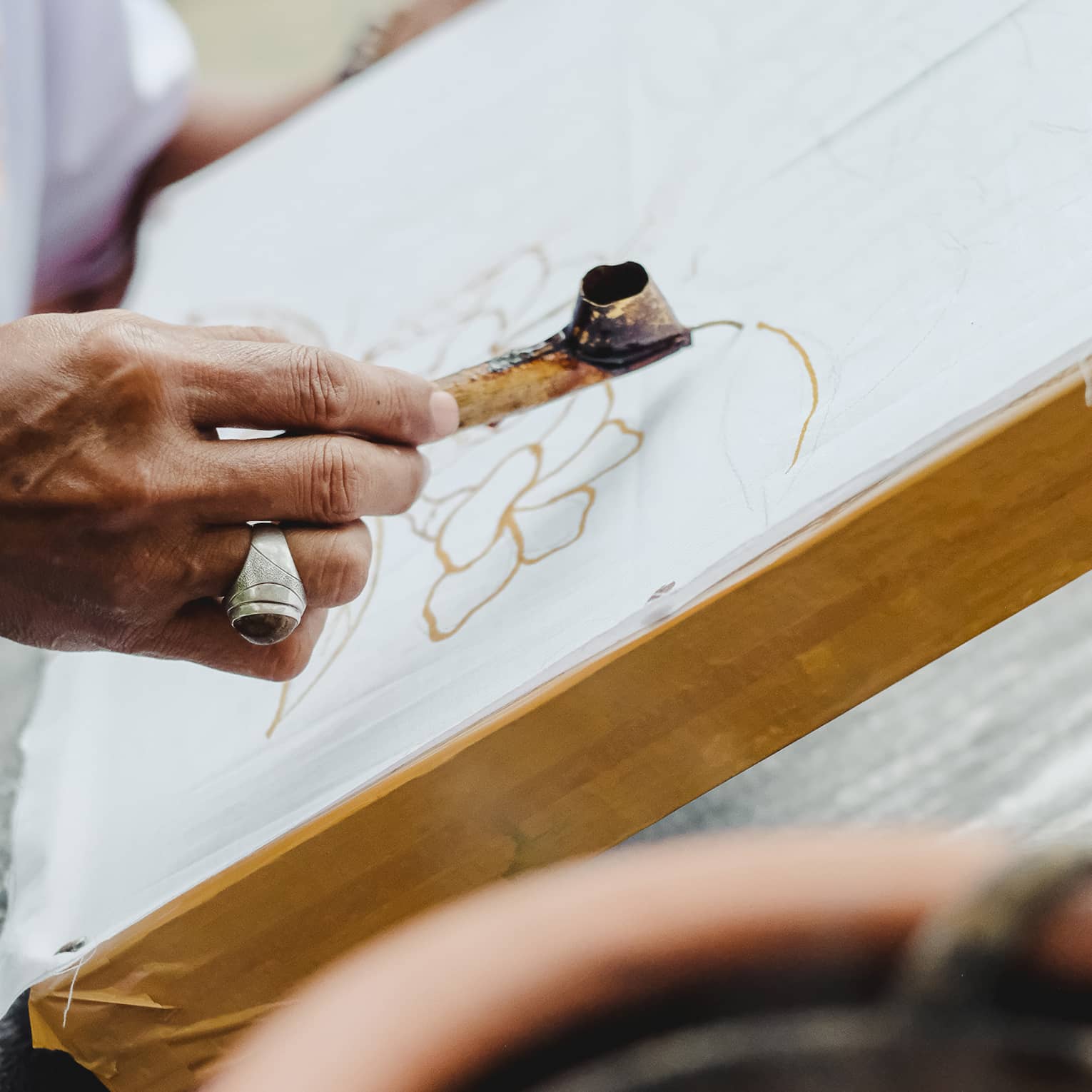 Close-up of someone using a metal Canting pen to draw a pattern in wax on a flat canvas.