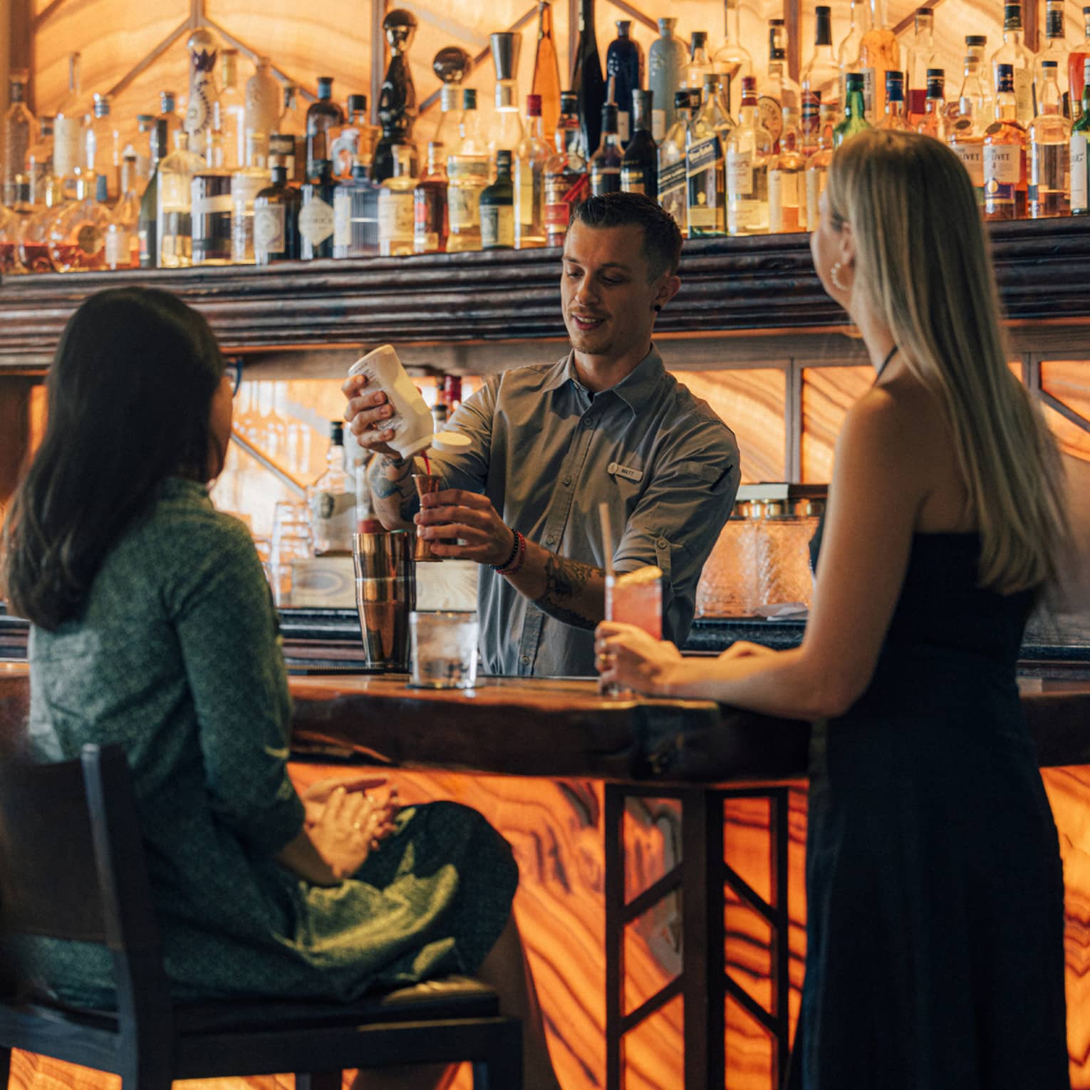 Two guests at the bar while the bartender is making a drink.