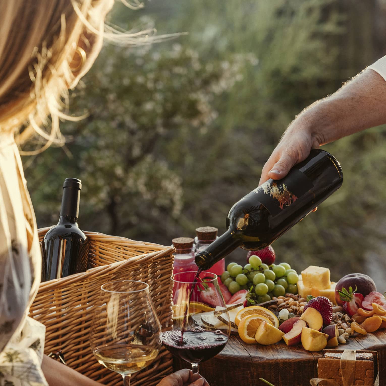 Guest eating a picnic outside with wine glasses and a fruit spread.