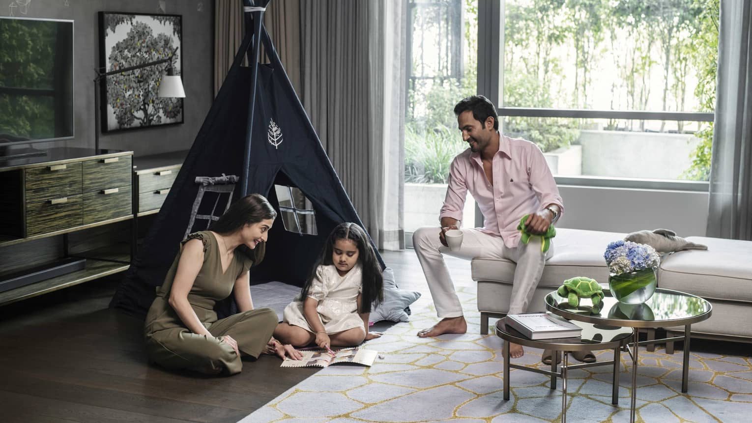 Mom, dad and young daughter relax in guest room with kids tent in background