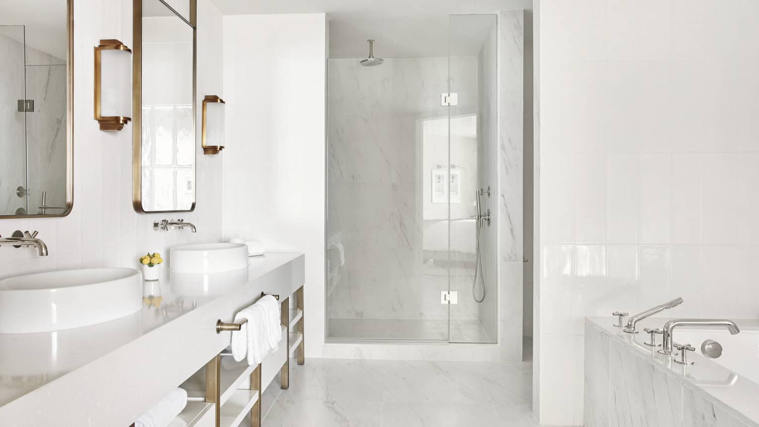 All white marble bathroom with double-sink vanity, shower with a glass door and a marble tub